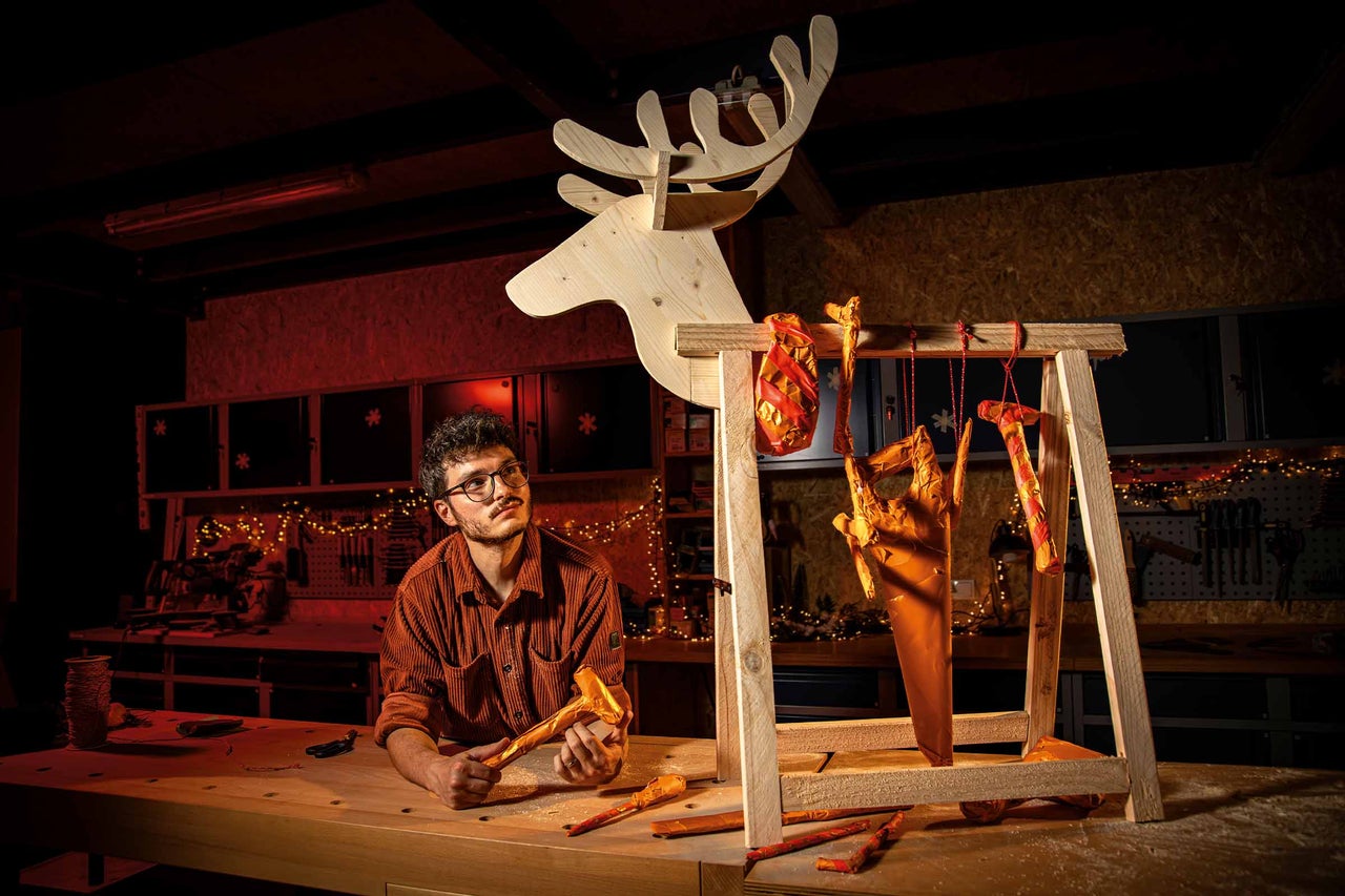 Homme regardant une décoration de renne en bois et des outils dans un atelier
