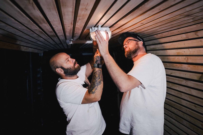 Zwei Männer montieren eine Lampe an einer Holzdecke.