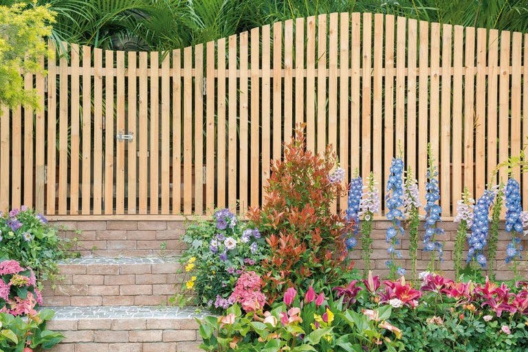 Clôture en bois avec parterre de fleurs devant un mur de pierre
