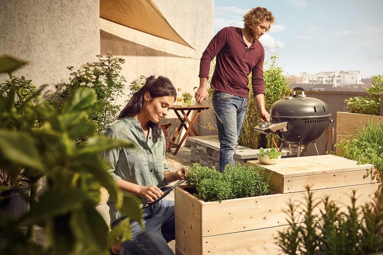 Des personnes jardinent et font des grillades sur un toit-terrasse avec des plates-bandes surélevées et un barbecue
