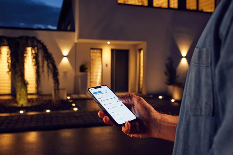 Une personne contrôle l'éclairage extérieur via une application pour smartphone à la maison