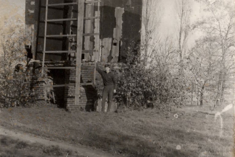Un homme se tient devant un bâtiment avec une maçonnerie en briques et une échelle en bois.