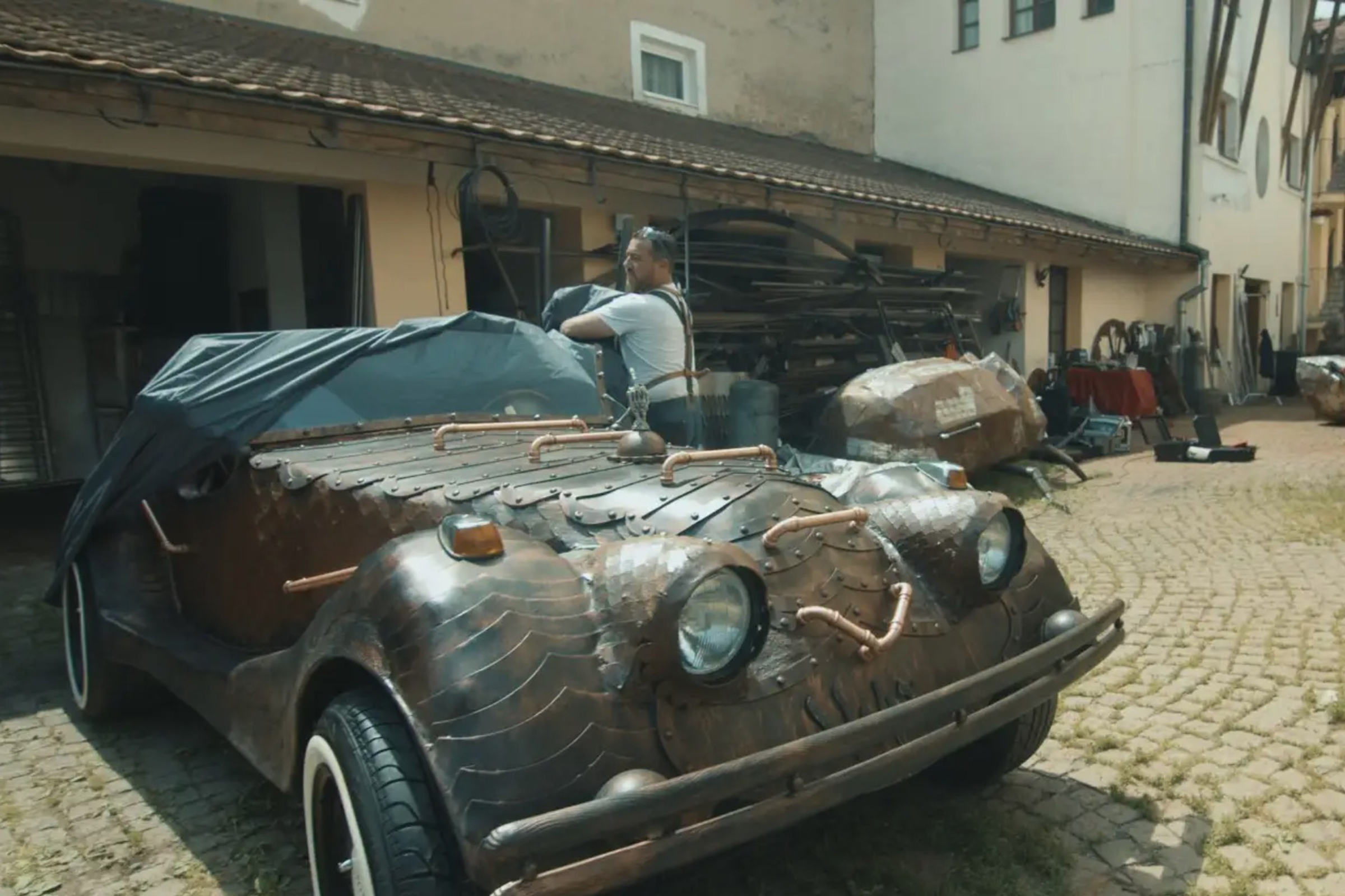 Ein individuell gefertigtes Auto mit Kupferdetails, teilweise mit einer Plane abgedeckt, steht im Freien.