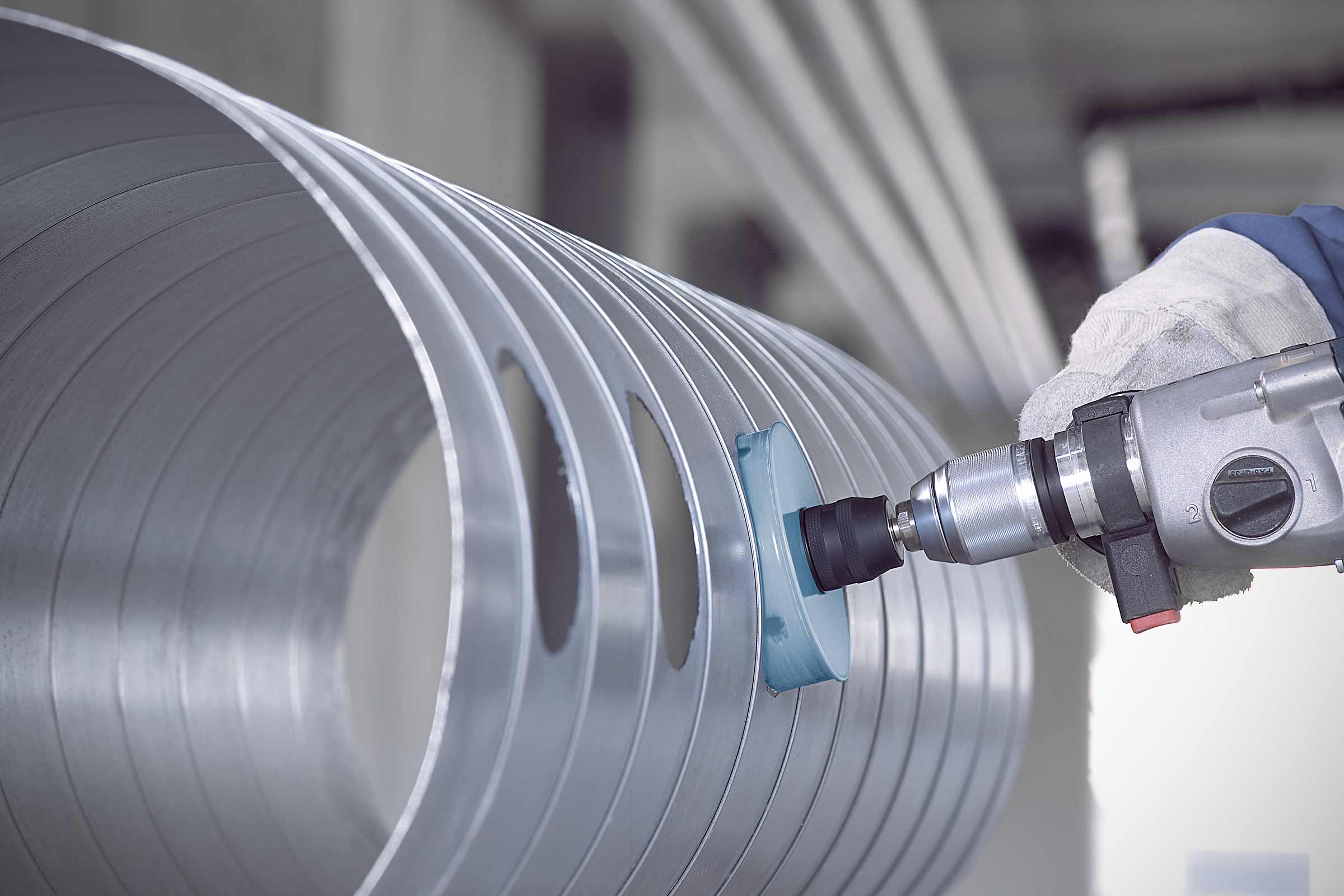 Outil de ponçage sur un tube en aluminium percé de trous, travaillé avec une perceuse