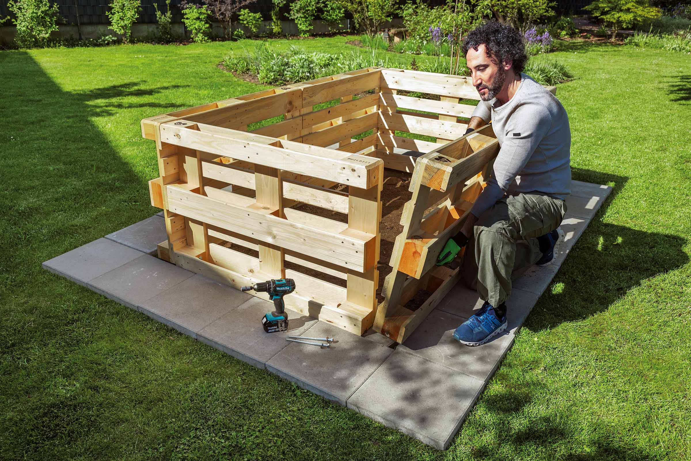 Mann baut einen Komposter aus Holzpaletten im Garten.