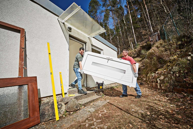 Deux personnes portent une porte devant une maison.