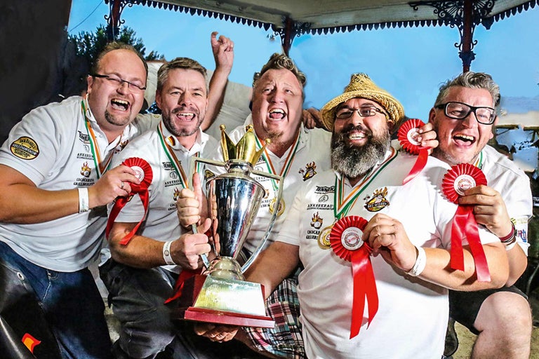 Cinq hommes célèbrent avec un trophée et des prix pour un concours de barbecue.