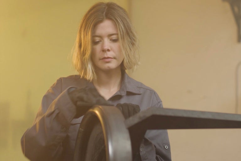 Frau reinigt Metallobjekt mit Handschuhen und Lappen