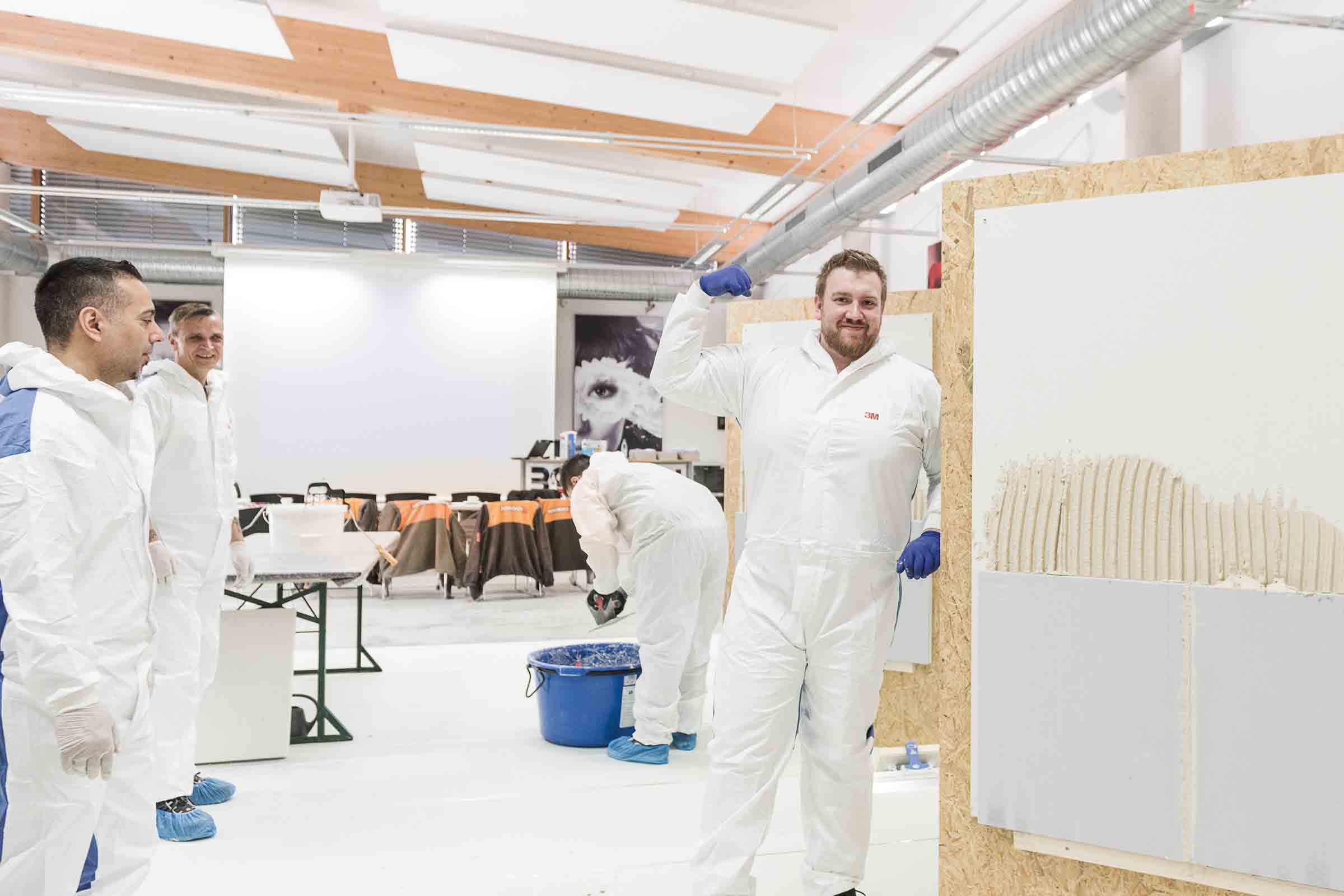 Photo d'intérieur d'une formation sur la maçonnerie avec des blocs de béton cellulaire avec plusieurs participants en combinaison de protection