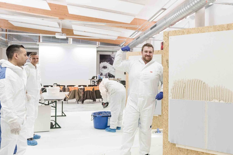 Innenaufnahme einer Schulung zum Thema Mauern mit Porenbetonsteinen mit mehreren Teilnehmern in Schutzanzügen