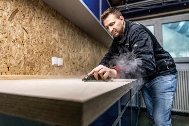 Ein Mann schleift eine Holzoberfläche in einer Werkstatt.