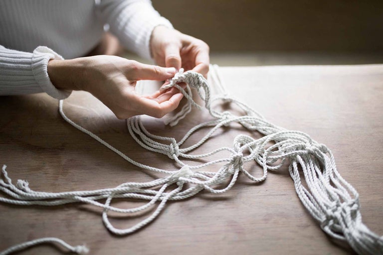 Nahaufnahme von Händen, die ein Makramee aus Seil knüpfen