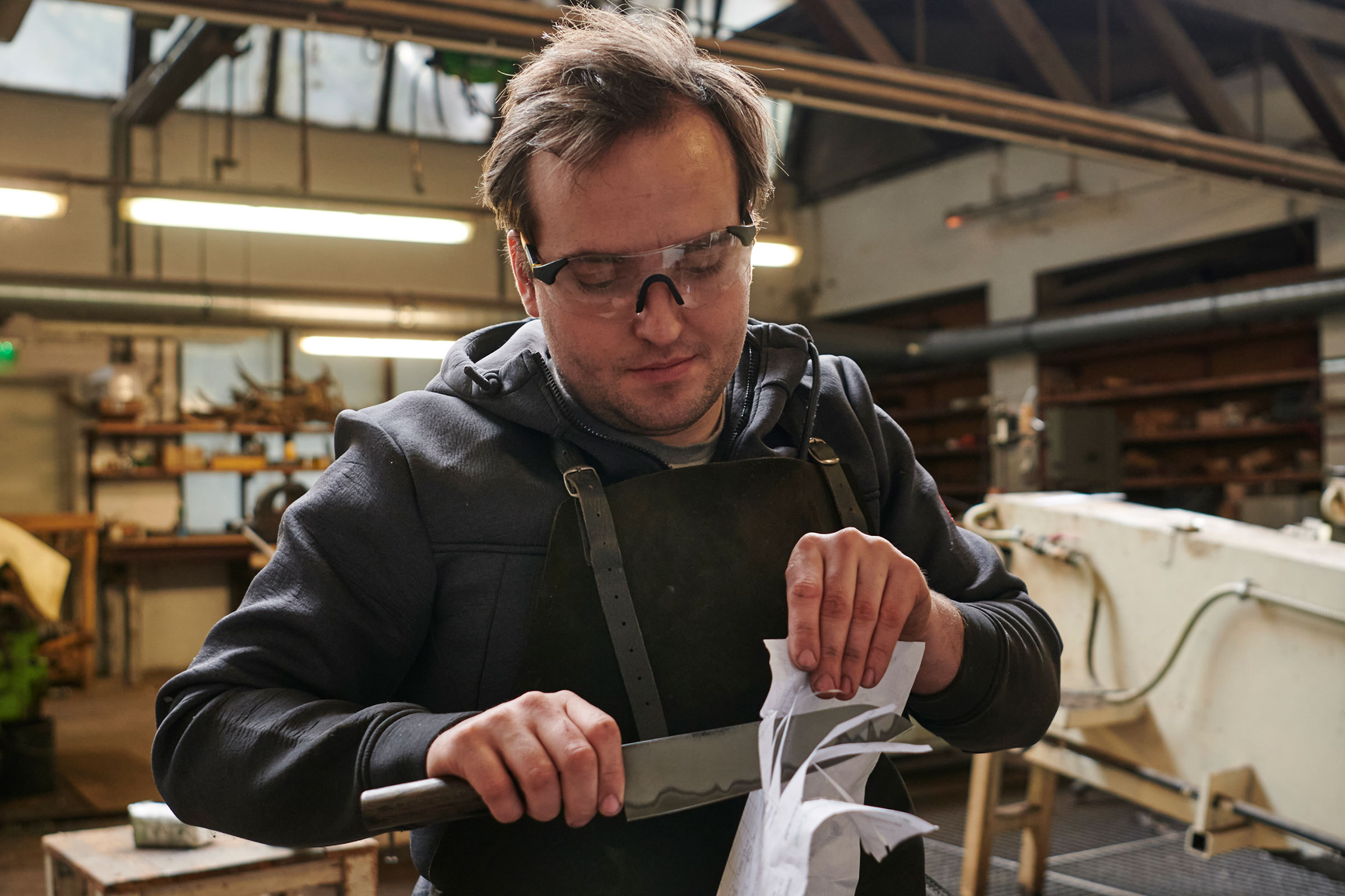 Mann mit Schutzbrille schärft Messer mit Papier