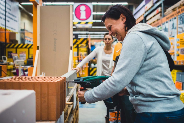 Une femme perce une brique avec une perceuse dans un magasin Hornbach.