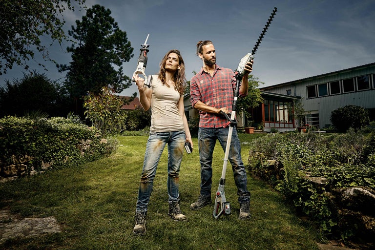 Ein Mann und eine Frau stehen mit einer Heckenschere und einer Säbelsäge in einem Garten.