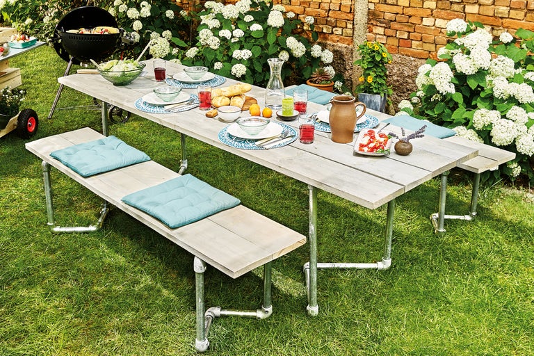 Table à manger dressée et bancs dans le jardin avec barbecue