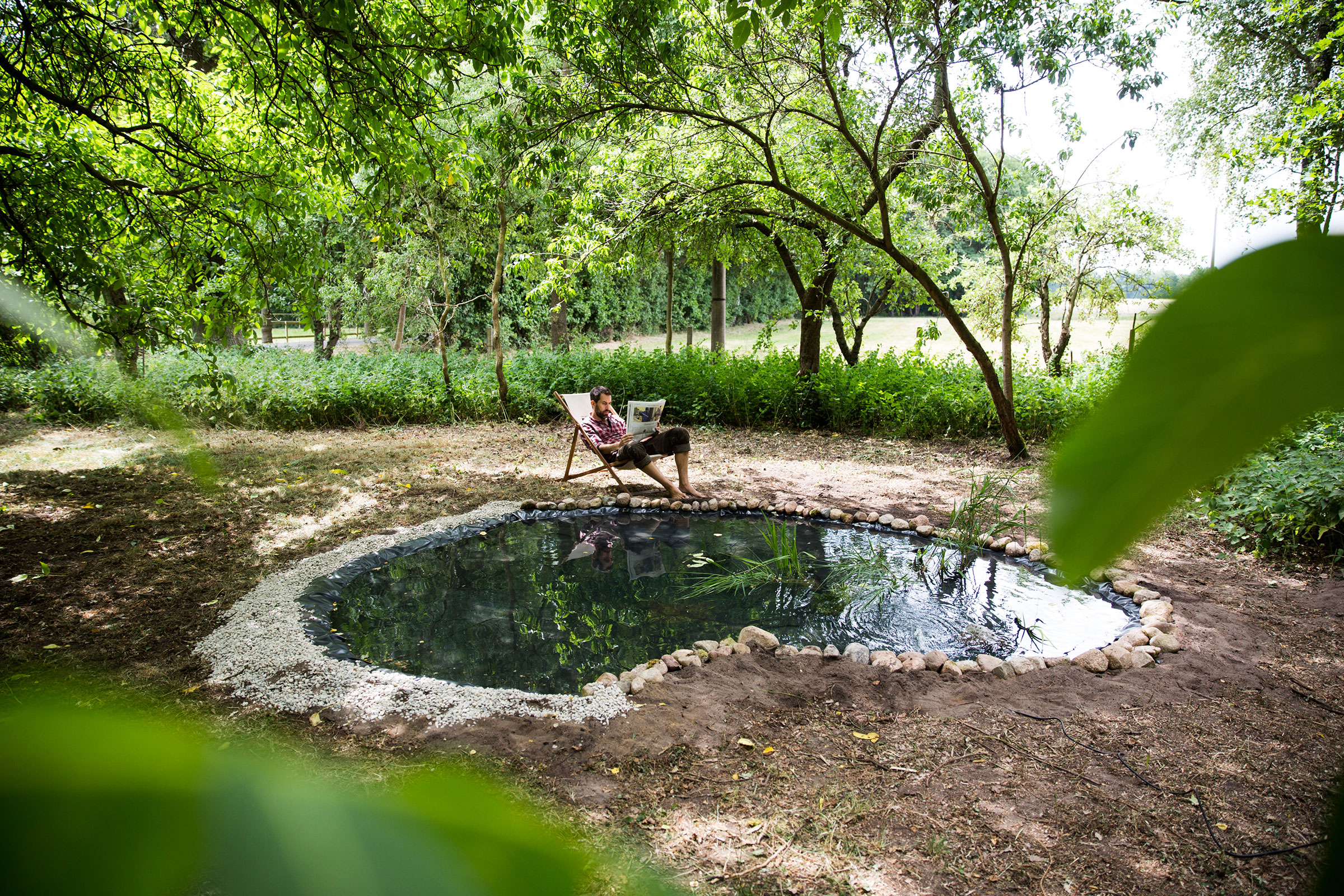 Gartenteich mit Ufergestaltung und entspanntem Mann im Liegestuhl
