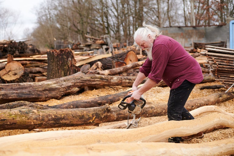Mann sägt Holz mit einer Kettensäge im Freien