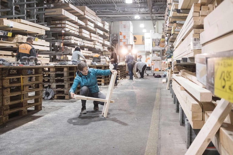 Une personne construit une chaise en bois dans une quincaillerie, avec des étagères en bois en arrière-plan.