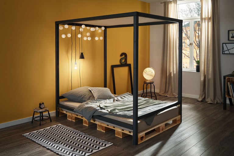 Chambre avec lit à baldaquin, cadre de lit en palettes et éclairage décoratif