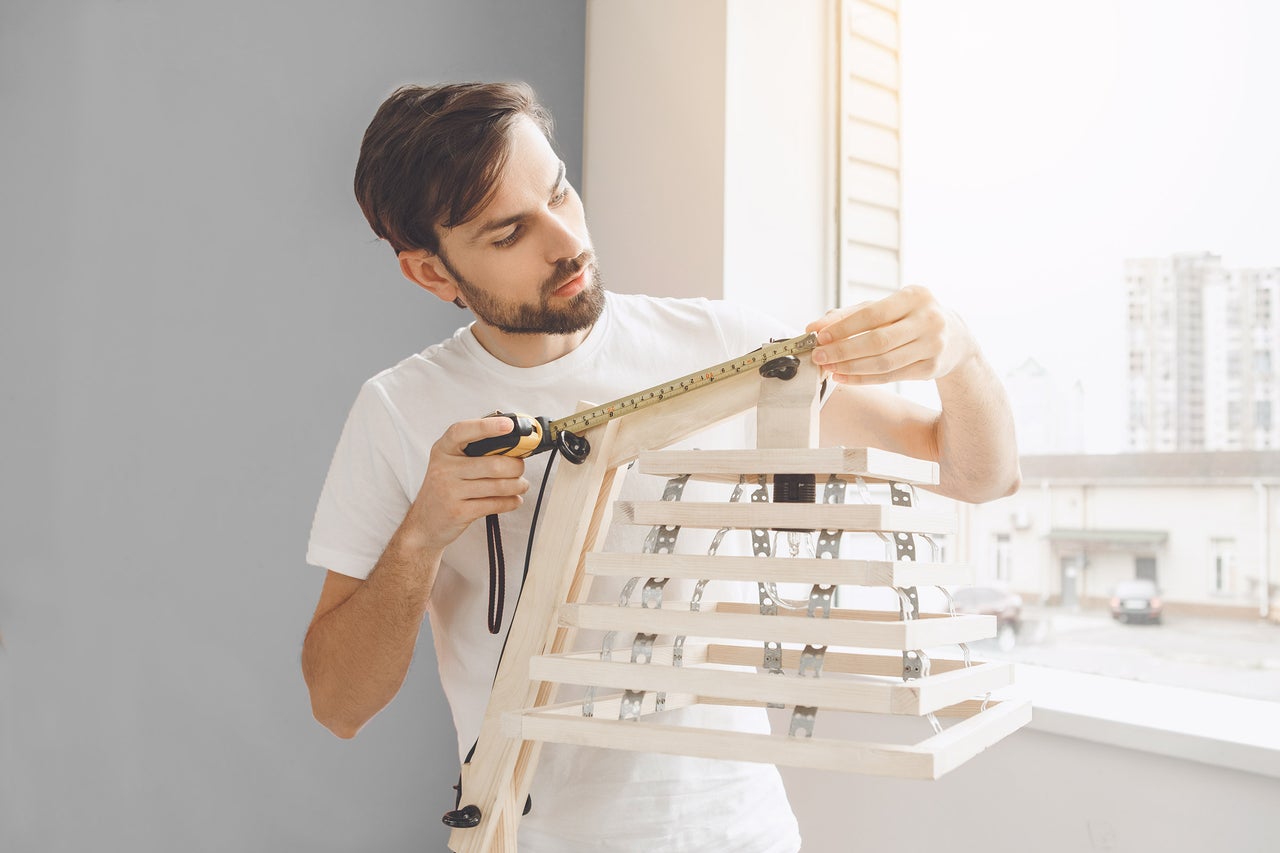 Un homme mesure une lampe en bois avec un mètre ruban.