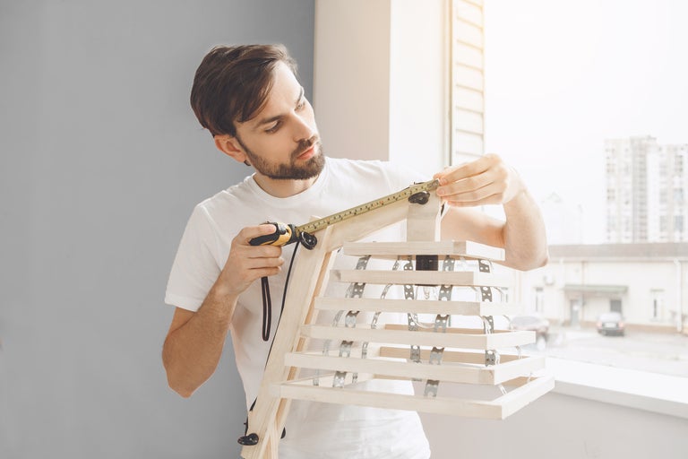 Un homme mesure une lampe en bois avec un mètre ruban.