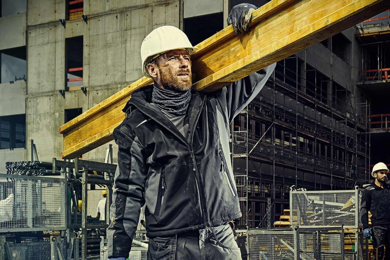 Ouvrier du bâtiment avec casque de protection transportant une poutre en bois sur un chantier