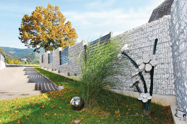 Clôture de gabions avec graminées ornementales et boule métallique dans le jardin