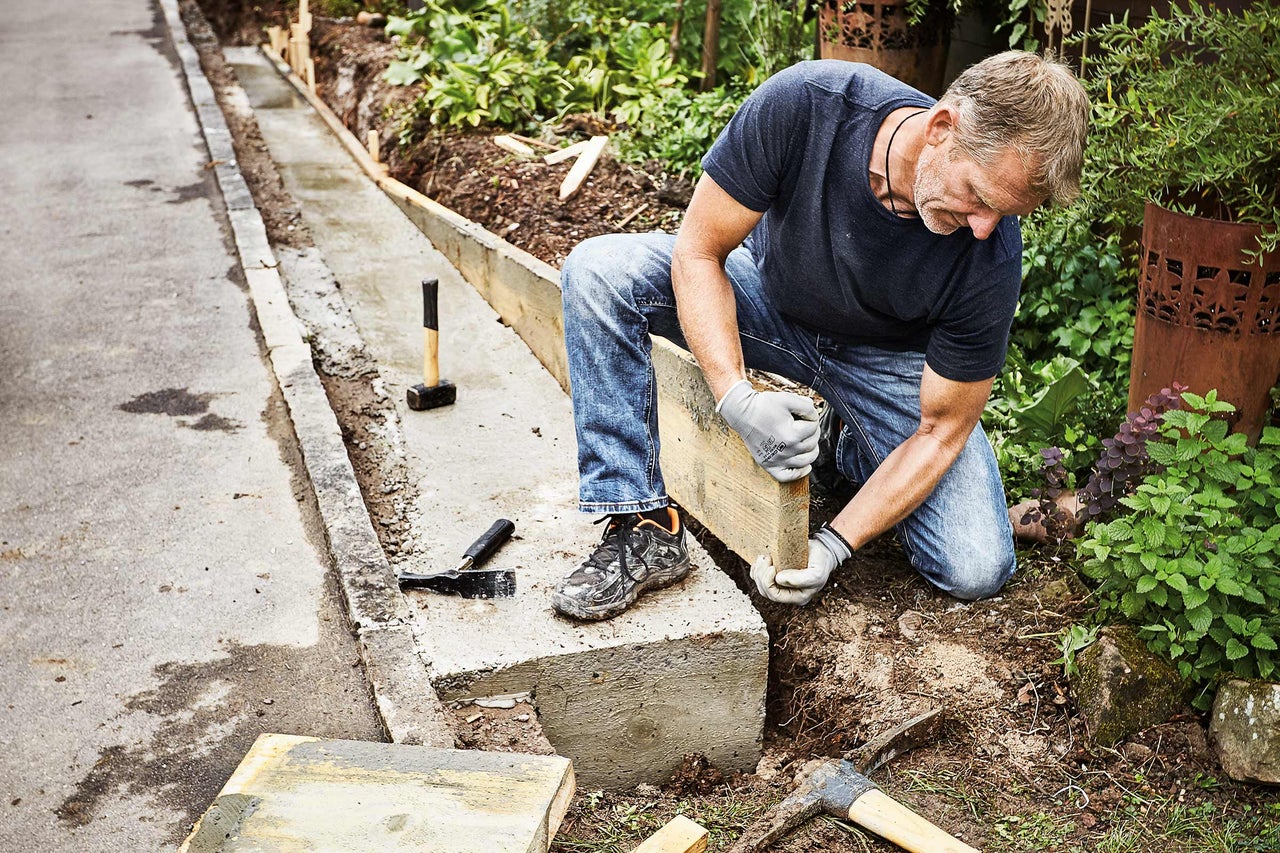 Mann arbeitet an einer Gartenlandschaft mit Betonbegrenzungen und Werkzeugen