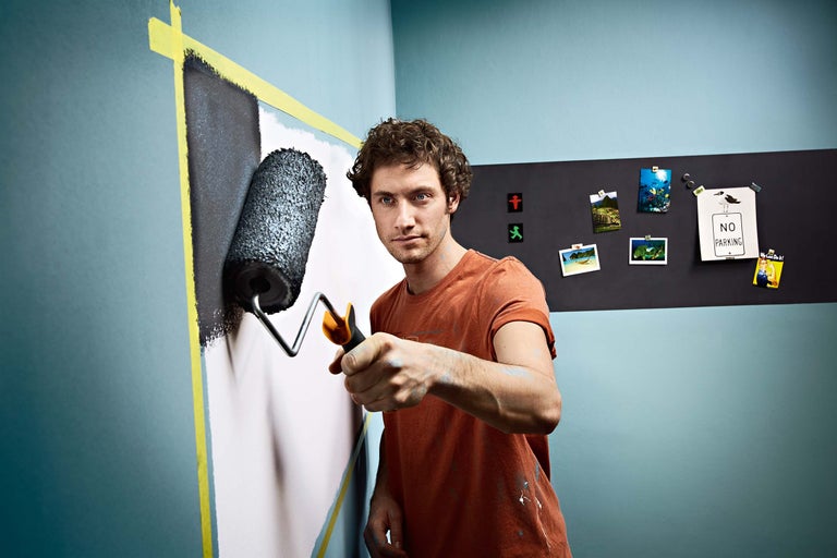 Mann streicht Wand mit Farbroller und Klebeband