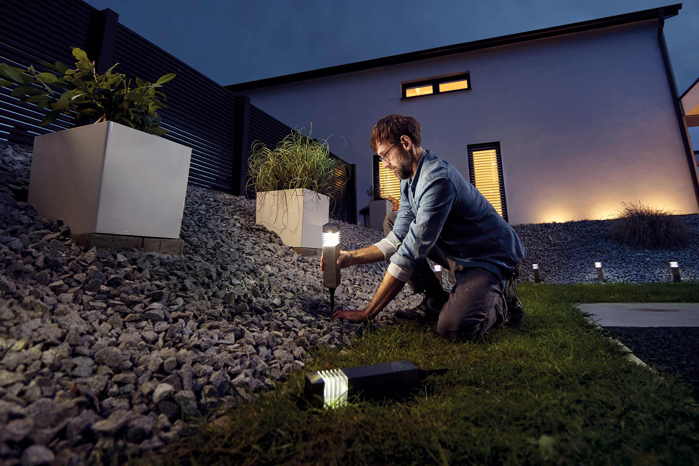 Ein Mann installiert eine Gartenleuchte in einem Garten mit Kies und Pflanzen