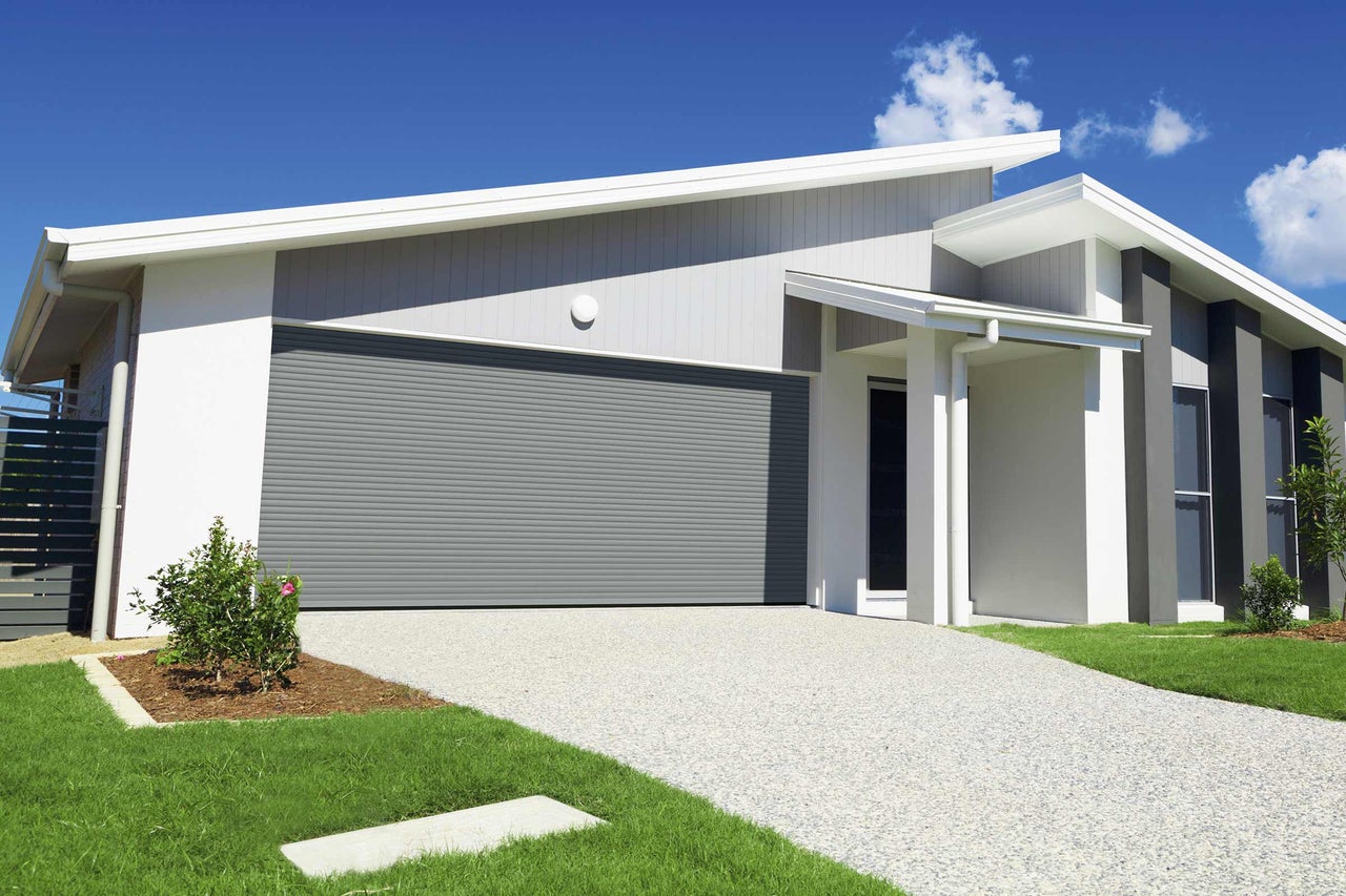 Ein modernes Haus mit einer grauen Rolltor Garage, einem gepflasterten Weg und einem gepflegten Garten.