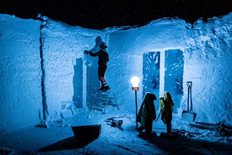 Bau einer Schneehütte mit Werkzeugen und Ausrüstung. Person steht auf einer Leiter.