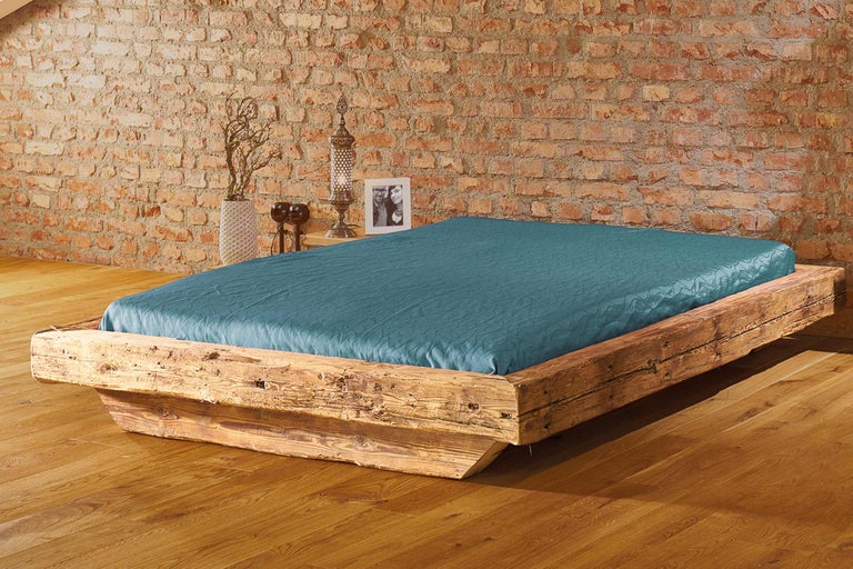 Lit avec cadre en bois et linge de lit bleu devant un mur en briques