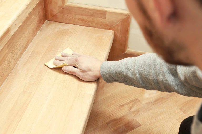 Homme ponçant un escalier en bois avec du papier de verre
