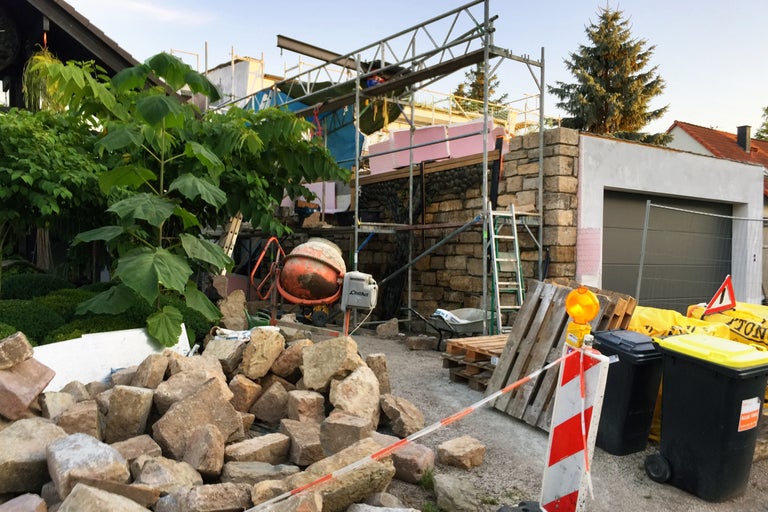 Baustelle mit Gerüst, Steinen, Betonmischer und Mülltonnen