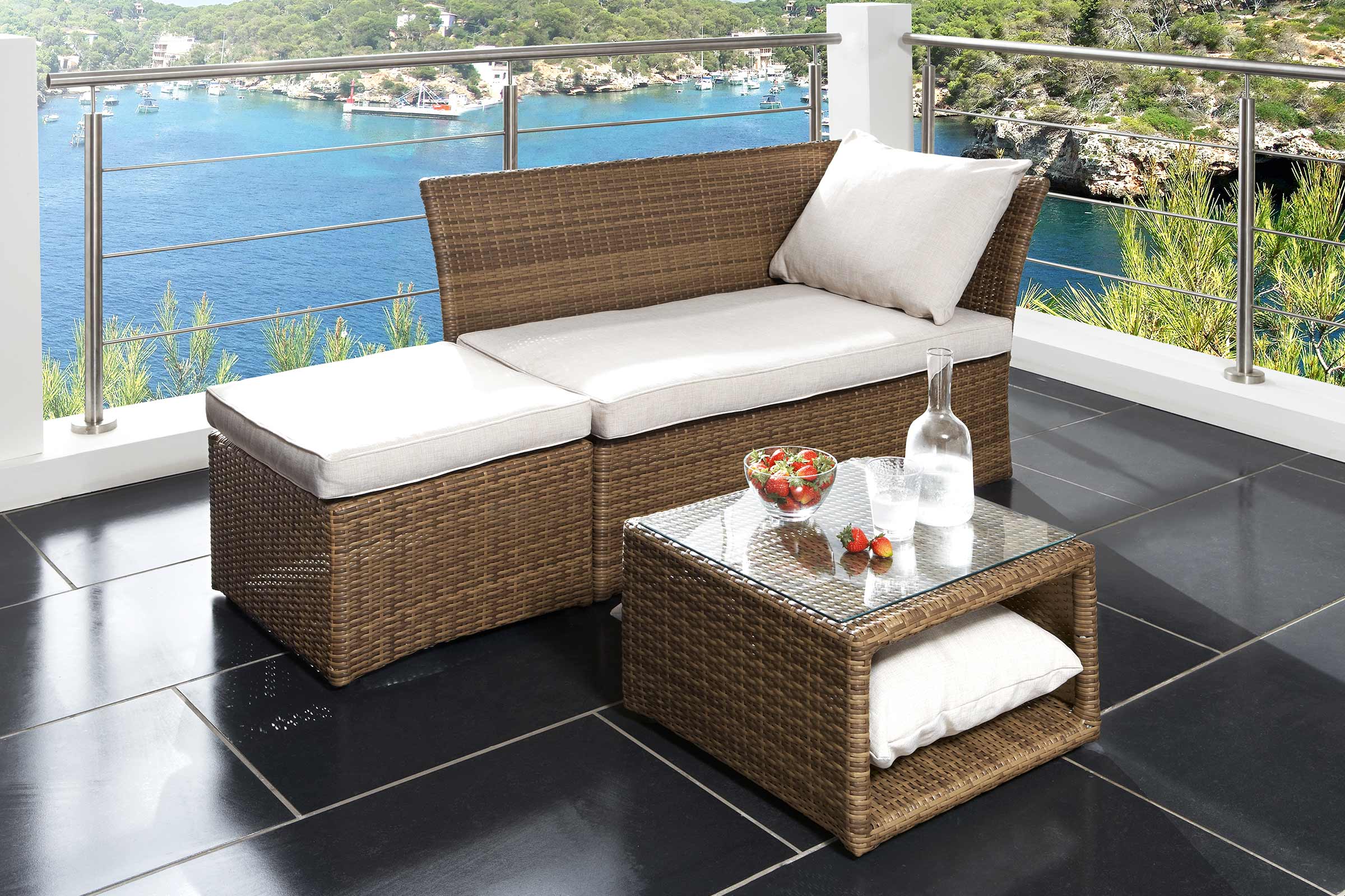 Terrasse mit Rattanmöbeln, bestehend aus Bank, Hocker und Tisch mit Glasplatte