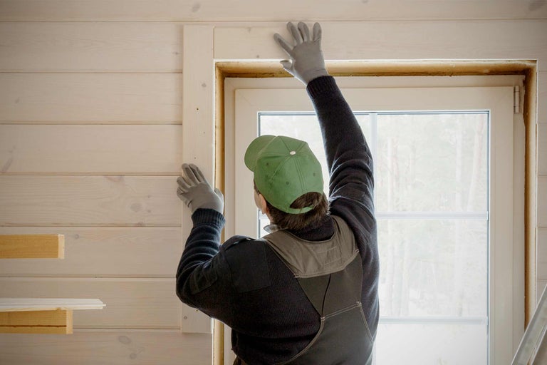 Artisan installant un cadre en bois autour d'une fenêtre dans une pièce avec des lambris.