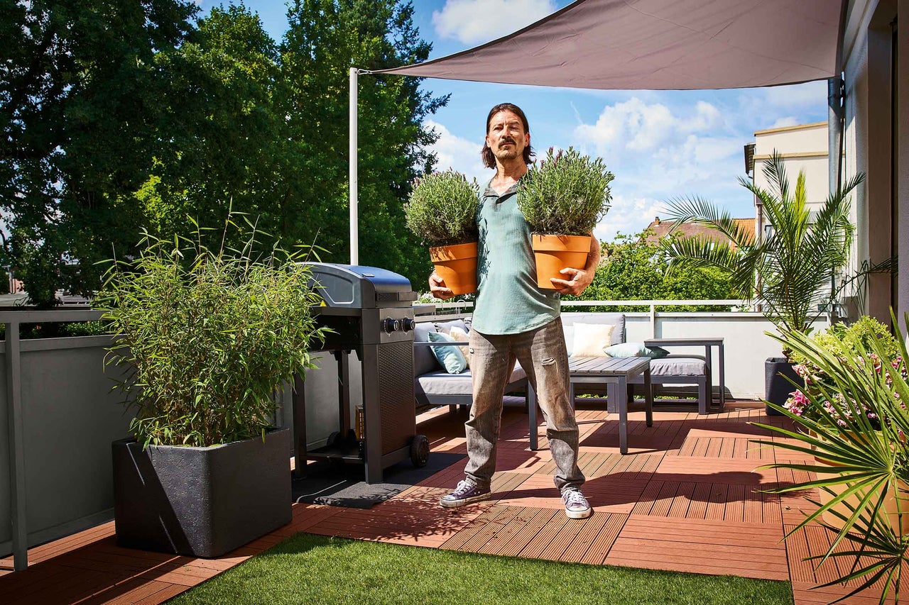 Une femme assemble un potager surélevé mobile en bois sur un balcon avec des outils et des plantes.