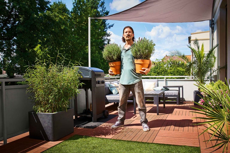 Une femme assemble un potager surélevé mobile en bois sur un balcon avec des outils et des plantes.