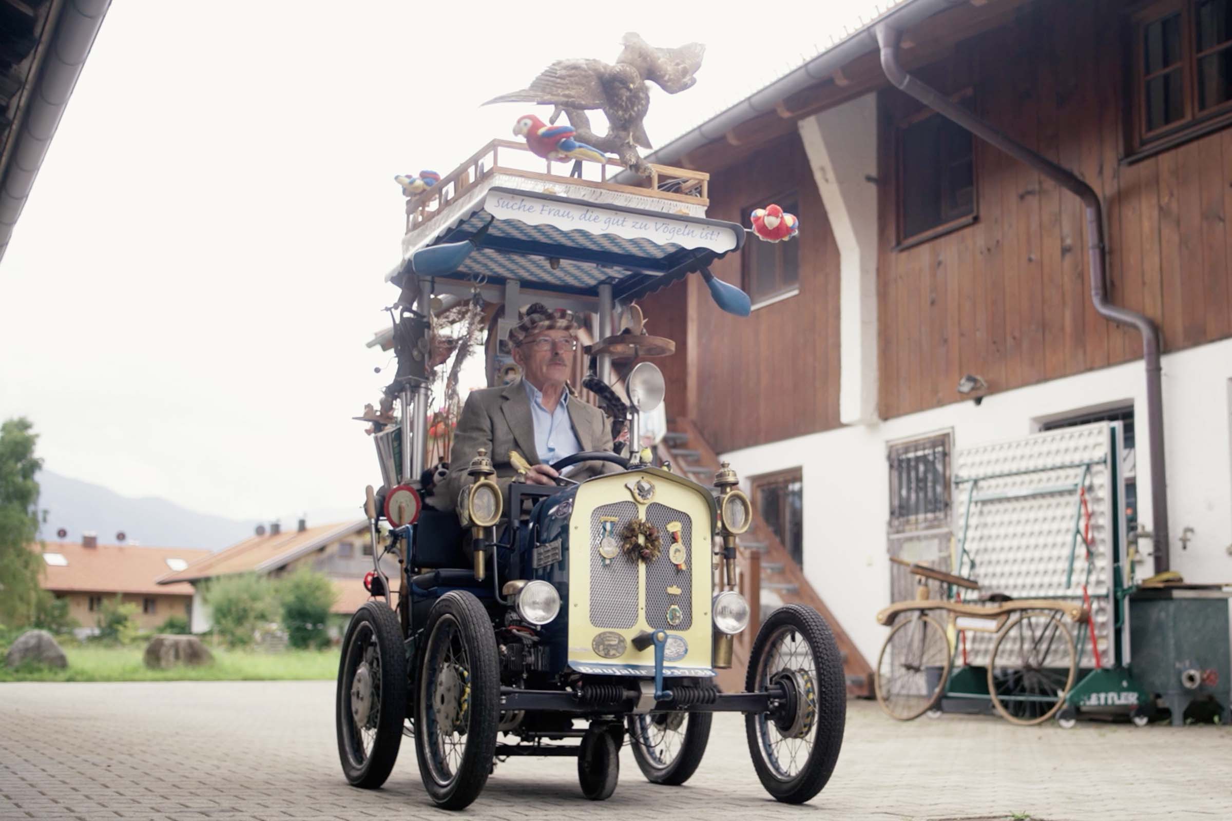 Ein Mann fährt ein dekoriertes Auto mit Vogelmotiven vor einem Haus.