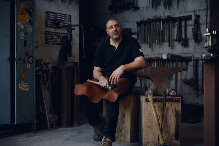 Schmied sitzt in Werkstatt mit Hammer und Amboss