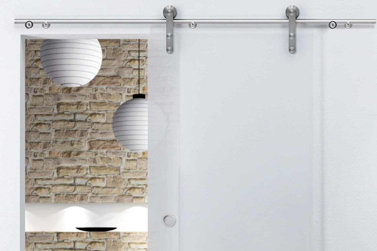 Porte coulissante en verre avec ferrures en acier inoxydable devant un mur en maçonnerie et des lampes en papier