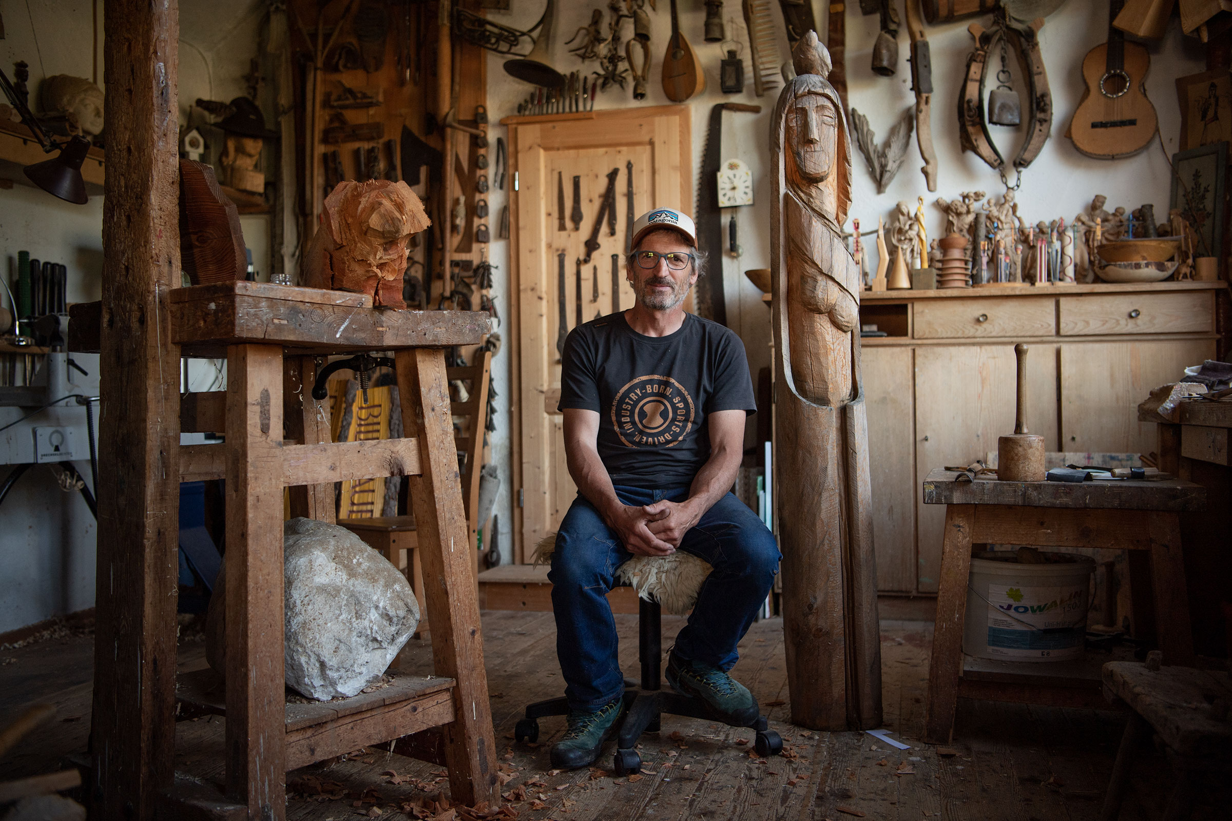 Werkstatt eines Holzbildhauers mit Skulpturen, Werkzeugen und einem sitzenden Mann