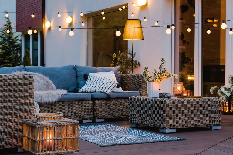 Terrasse avec canapé en rotin, table basse et guirlande lumineuse pour une ambiance chaleureuse