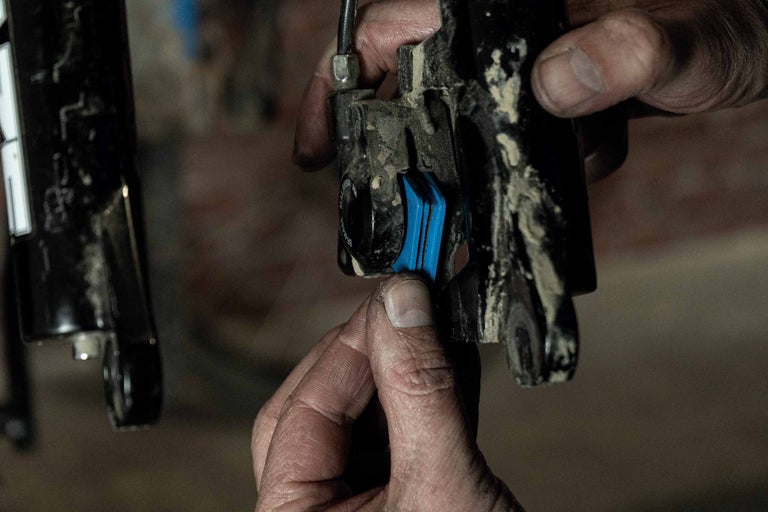 Nahaufnahme einer Person, die blaue Bremsbeläge an einer Fahrradbremse montiert.