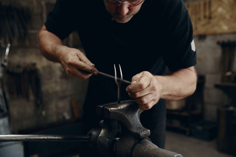 Ein Mann bearbeitet Metall mit einer Feile in einem Schraubstock. Schmiedearbeiten.