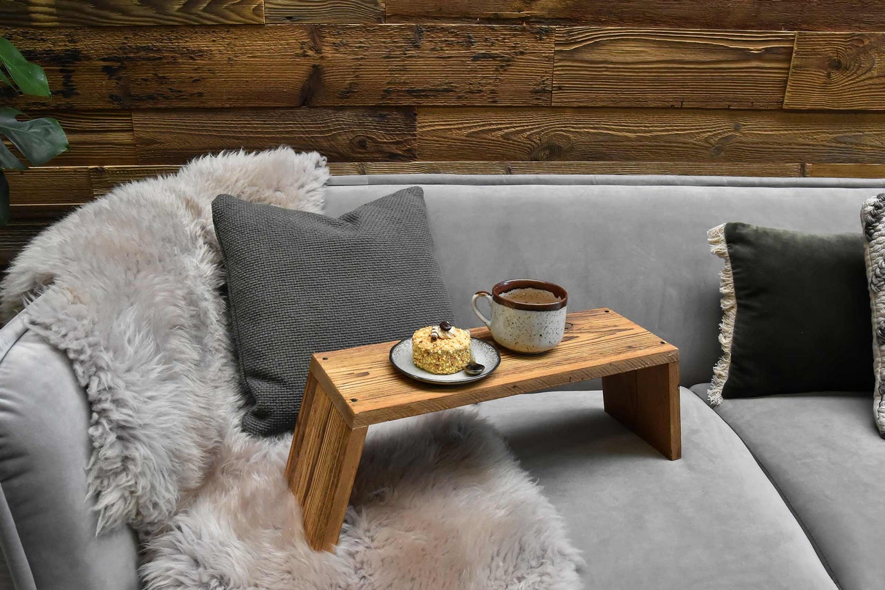 Scène avec plateau, tasse, gâteau et coussins sur un canapé devant un mur en bois