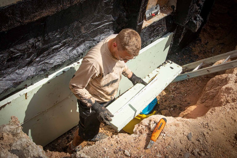 Un homme pose des panneaux isolants pour l'étanchéité d'une cave dans le sol