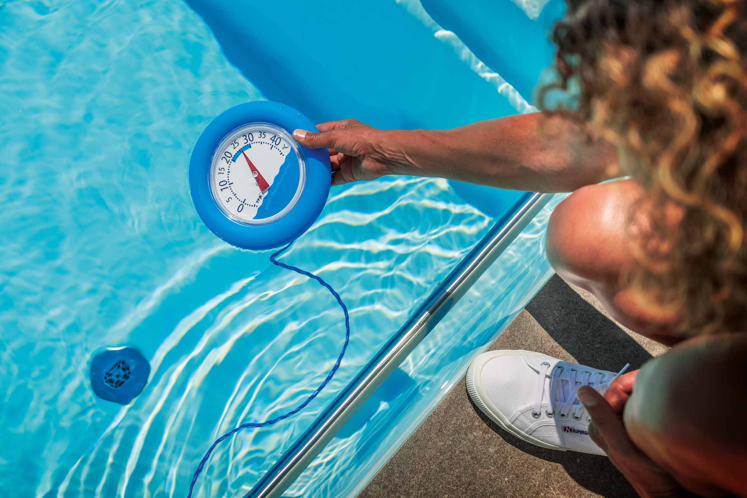 Eine Person misst die Temperatur in einem Pool mit einem Poolthermometer.